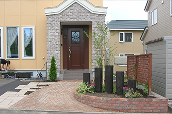 カーブを描くレンガと枕木で作られた花壇のあるアプローチ空間